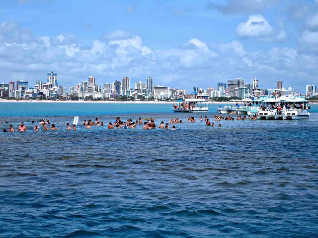 Banhistas nas piscinas naturais de Picãozinho, com os prédios da orla de João Pessoa ao fundo