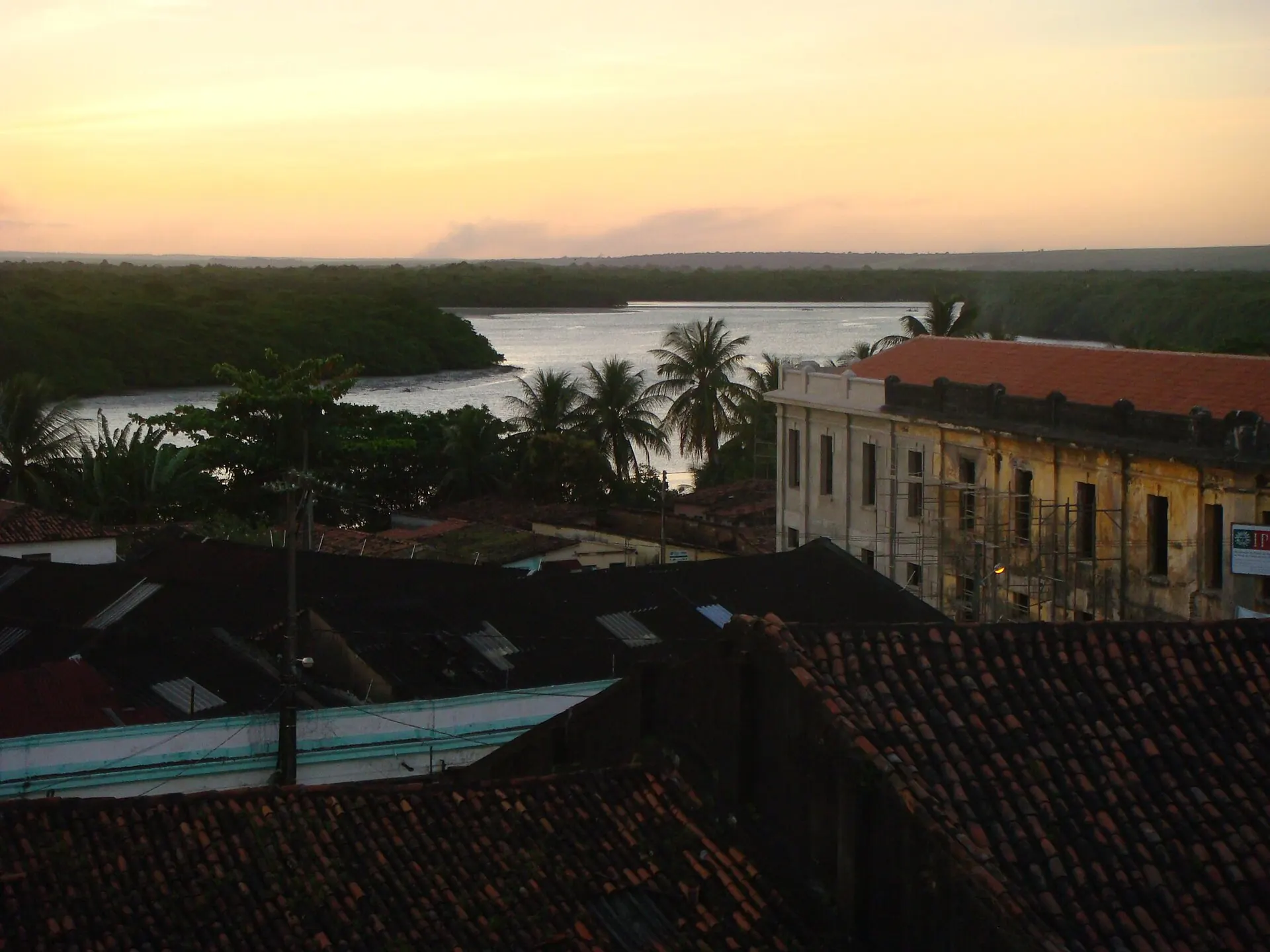 Céu claro de fim de tarde sobre os telhados do Varadouro, um casarão antigo, coqueiros e o rio Sanhauá entre o mangue, visto do alto do Centro Histórico