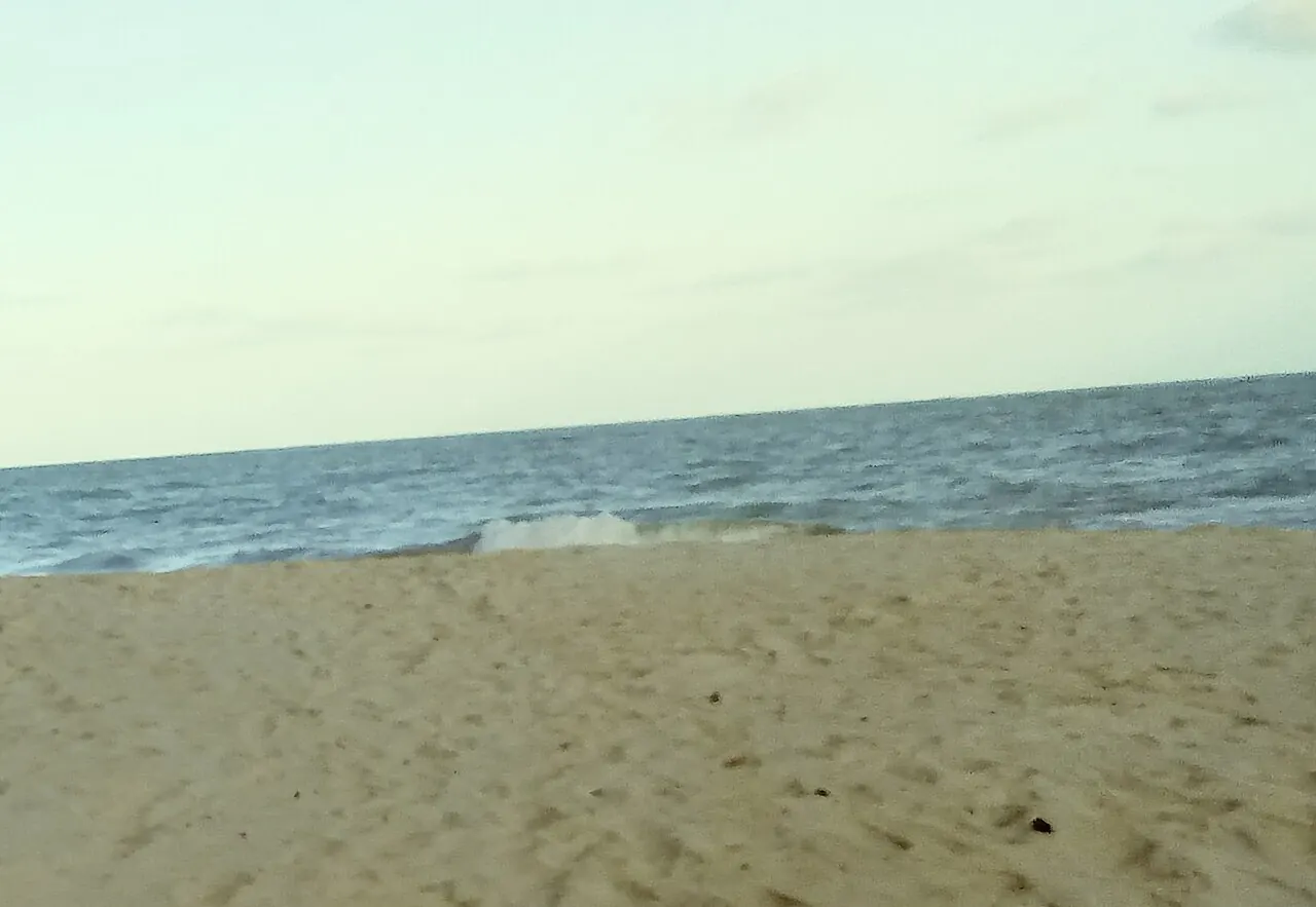 Faixa de areia clara da Praia de Jacarapé e o mar com ondas fracas sob céu claro