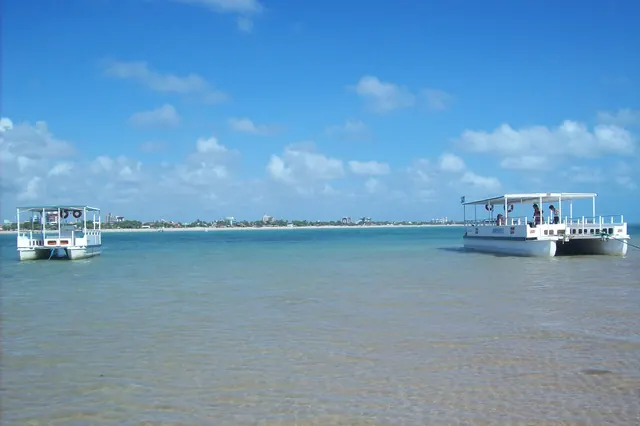 Dois catamarãs parados na água rasa de Areia Vermelha, com a orla de Cabedelo ao fundo