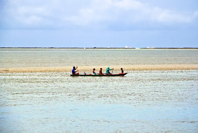 Canoa com quatro pessoas remando na água rasa do estuário do Mamanguape
