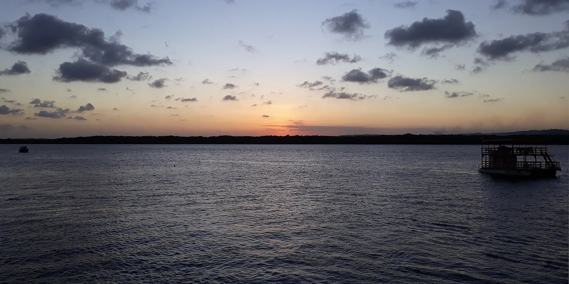 Anoitecer no rio Paraíba na Praia do Jacaré, com uma embarcação parada na água