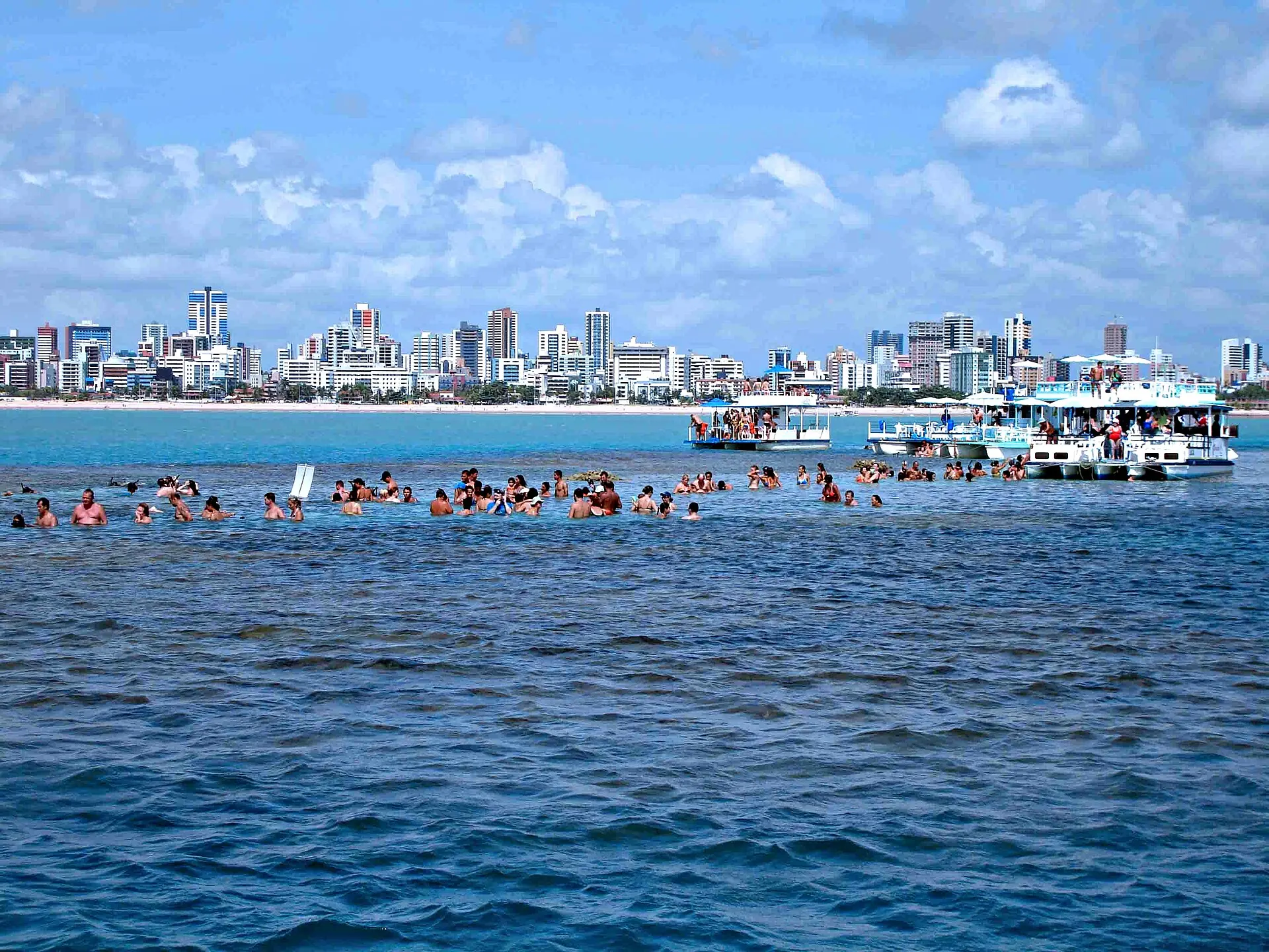 Banhistas nas piscinas naturais de Picãozinho, com os prédios da orla de João Pessoa ao fundo