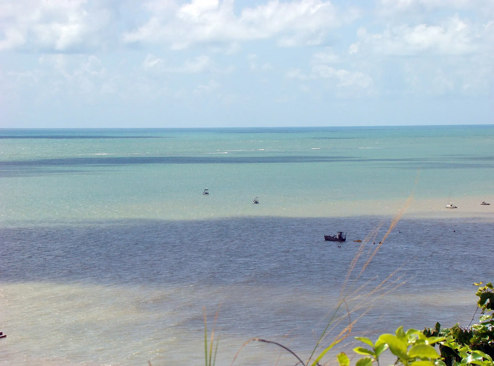 Mar raso e esverdeado em frente à Ponta do Seixas, com um barco ao longe